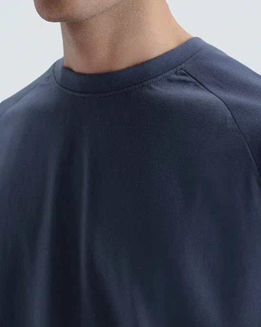 Close-up of a person wearing a dark navy blue crew-neck t-shirt, showing the collar, shoulder seam, and chest area against a light gray background.