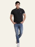 Man wearing a black patterned polo shirt and blue jeans on a white background Black Dotted Regular Fit Men’s Polo T-Shirt Royal Outfits POLO T Shirts - Black Dotted Regular Fit Men’s Polo T-Shirt - Royal Outfits - POLO T Shirts - Black Dotted Regular Fit Men’s Polo T-Shirt - Royal Outfits