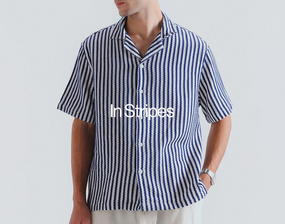 A man wearing a short-sleeve button-up shirt with vertical blue and white stripes, shown from the neck down against a light gray background. The text 'In Stripes' is overlaid across the chest.