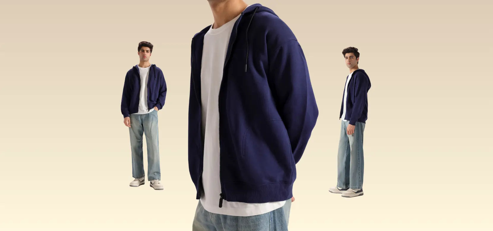 Person wearing a navy blue hoodie and light blue jeans standing against a beige background.