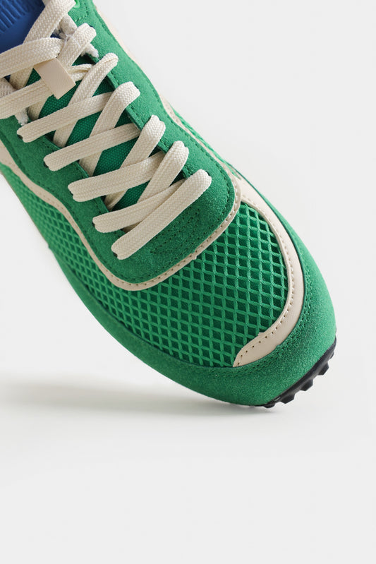 Green sneaker with white laces on a light gray background