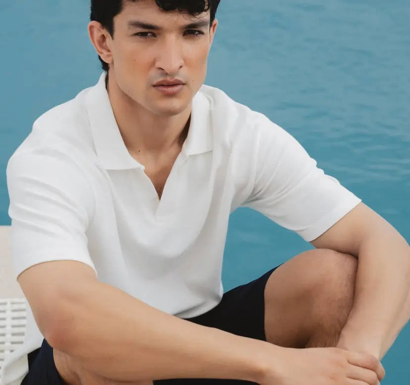 Man wearing a white polo shirt and black shorts sitting by a body of water.
