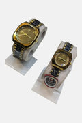 Two gold and black watches on white stands with a visible brand logo (Couple's).