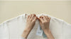 Person holding a white shirt with a tag labeled 'CLOTH' against a beige background