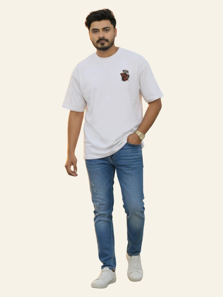 Man wearing a white t-shirt with a logo and blue jeans on a light gray background Graphic White Drop Shoulder "Dhool" T-Shirt Royal Outfits Drop Shoulder T-Shirts