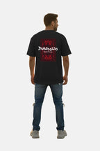 Man wearing a black t-shirt with a red and white graphic design on the back, standing against a plain background. Graphic Black Drop Shoulder Dimension T-Shirt Royal Outfits Drop Shoulder T-Shirts - Graphic Black Drop Shoulder Dimension T-Shirt - Royal Outfits - Drop Shoulder T-Shirts