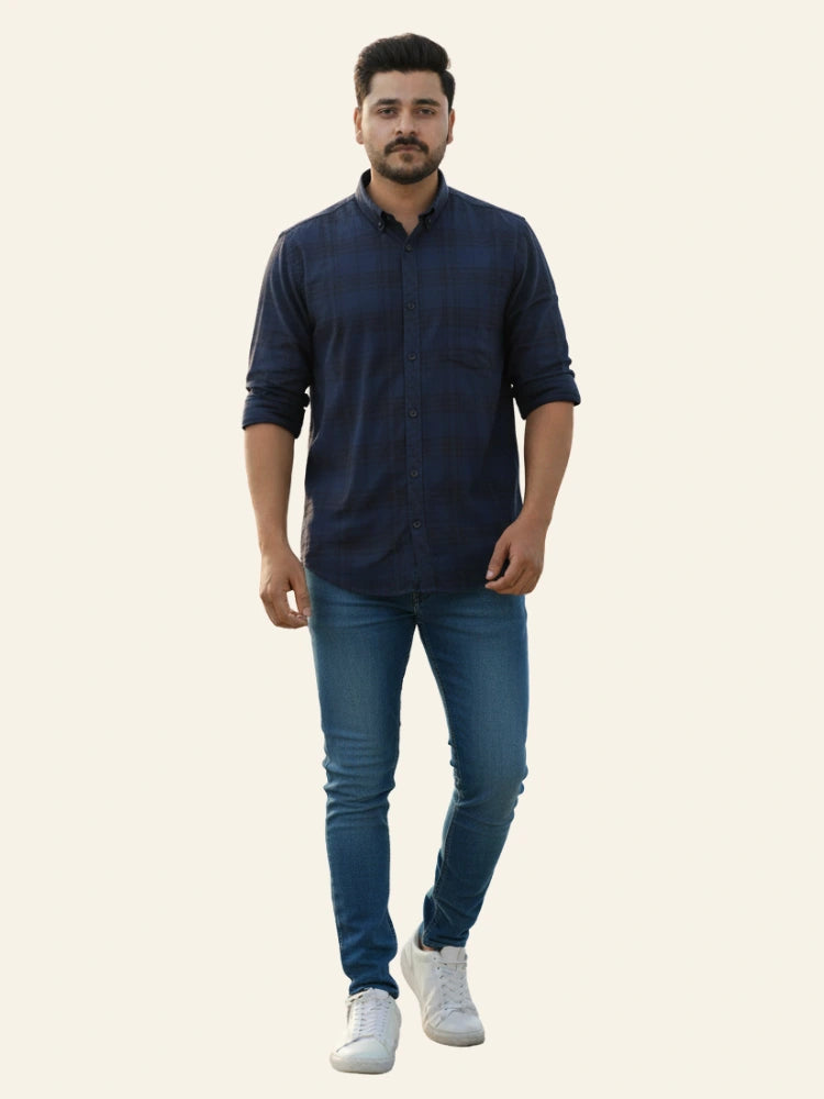 Man wearing a navy blue shirt and jeans on a plain background