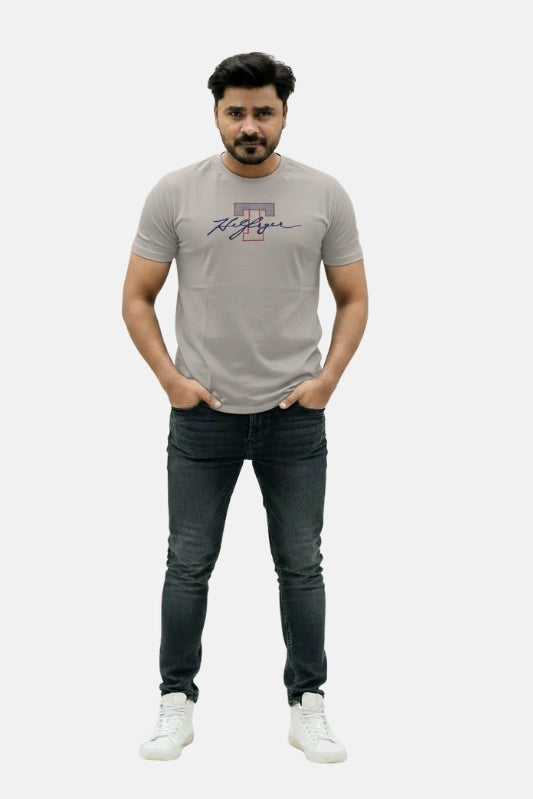 Man wearing a gray t-shirt with a logo and dark jeans on a white background Light Grey T Hedges T-Shirt Royal Outfits Printed T Shirts - Light Grey T Hedges T-Shirt - Royal Outfits - Printed T Shirts - Light Grey T Hedges T-Shirt - Royal Outfits