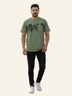 Man wearing a green t-shirt with black text pattern and black pants on a white background