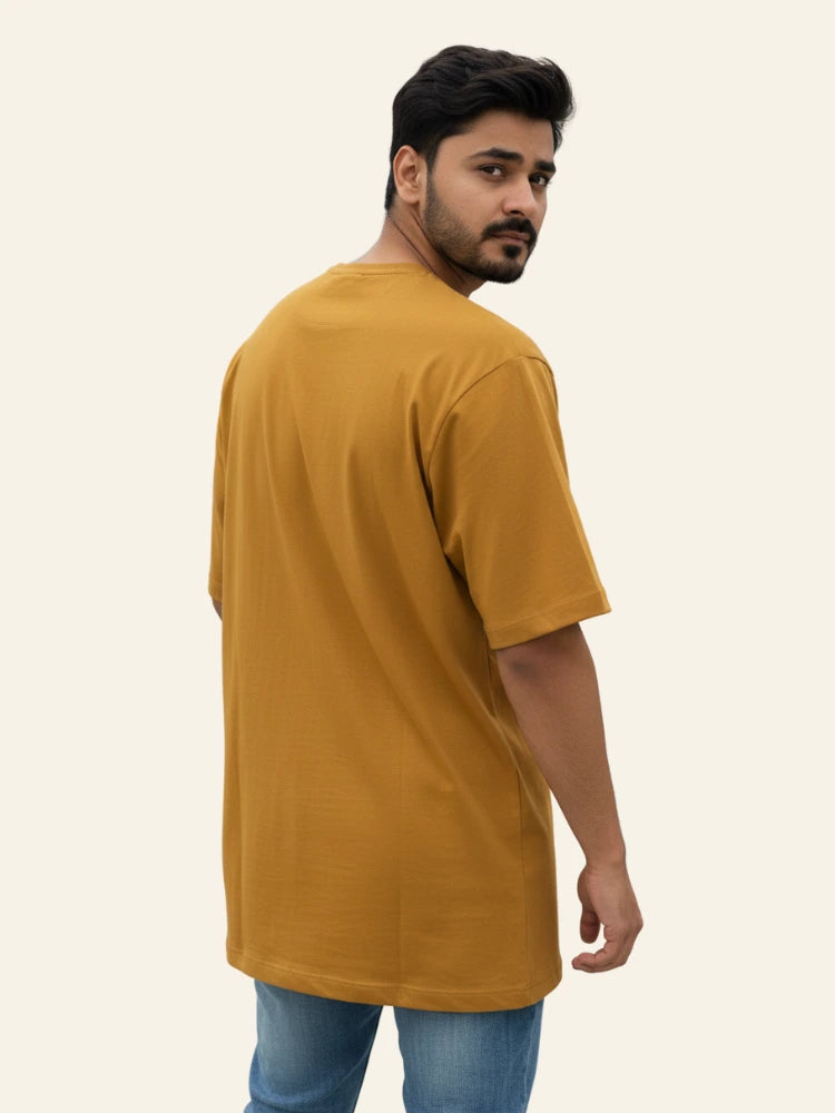 Man wearing a mustard t-shirt on a plain background
