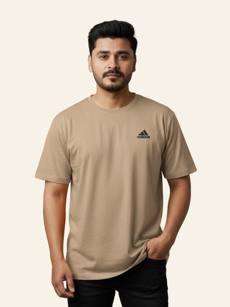 Man wearing a beige Adidas t-shirt on a plain background