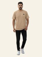Man wearing a beige Adidas t-shirt and black pants on a white background