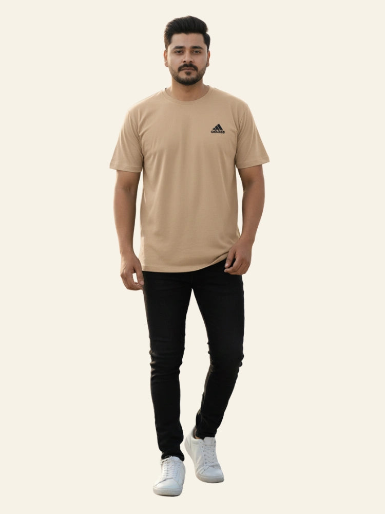 Man wearing a beige Adidas t-shirt and black pants on a white background