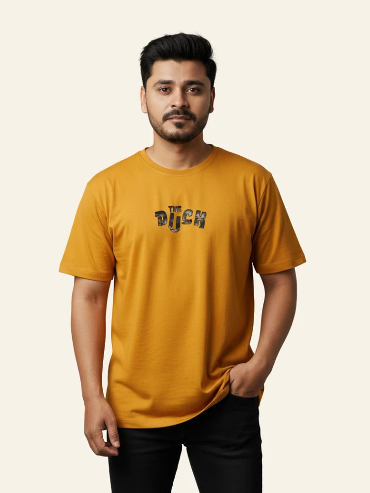 Man wearing a mustard yellow t-shirt with text on a beige background