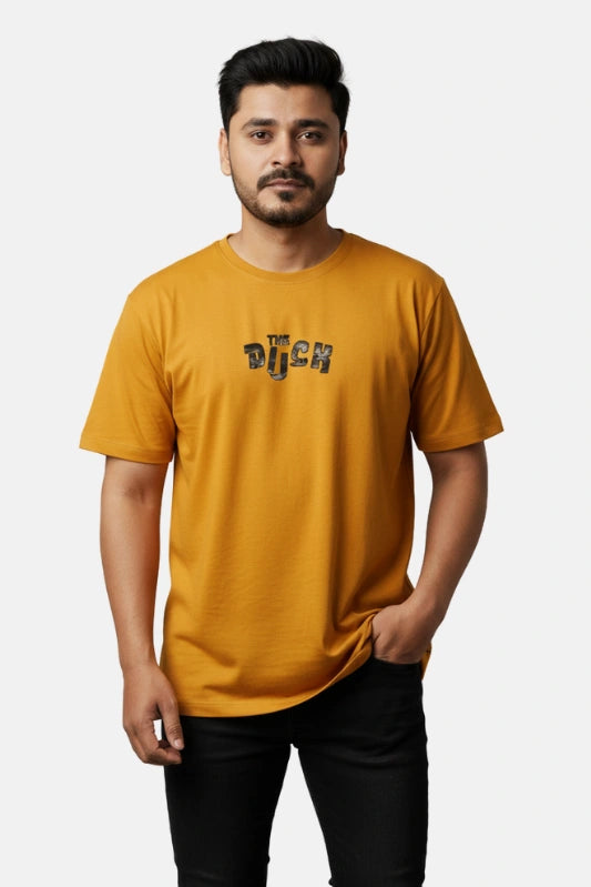 Man wearing a mustard yellow t-shirt with text on a beige background - Graphic Mustard Drop Shoulder The Duck T-Shirt - Royal Outfits - Drop Shoulder T-Shirts - Graphic Mustard Drop Shoulder The Duck T-Shirt - Royal Outfits