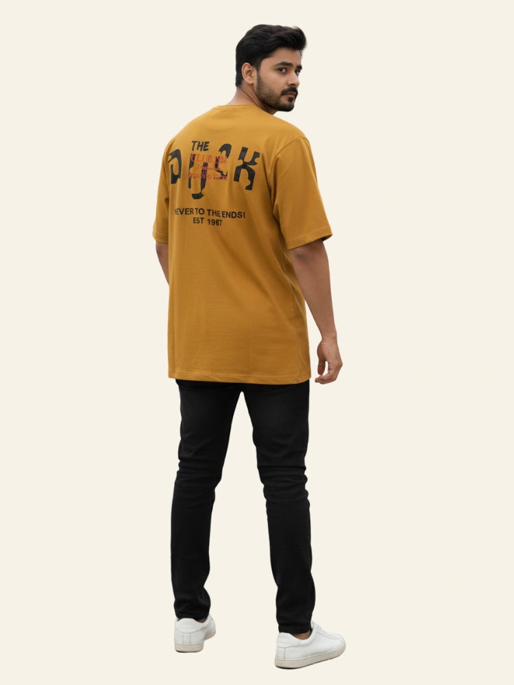 Man wearing a mustard yellow t-shirt with text on the back, standing against a white background