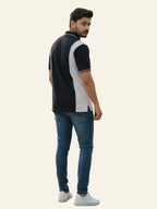 Man wearing a black and white polo shirt with blue jeans on a light gray background