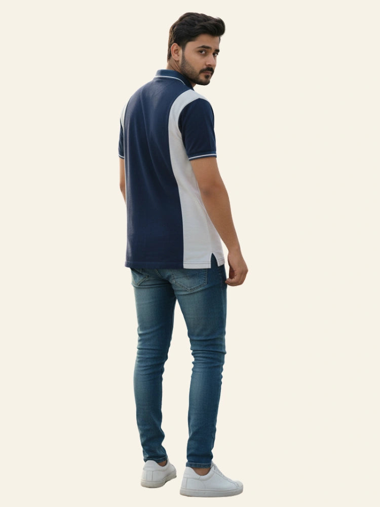 Man wearing a navy and white polo shirt with blue jeans on a beige background