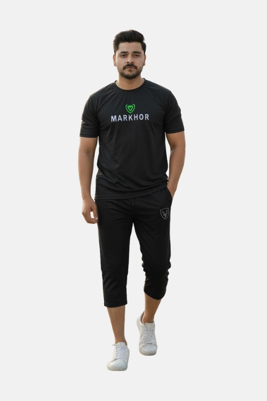 Man wearing a black 'Markhor' branded outfit on a beige background - Black 'Markhour' Tracksuit - Royal Outfits - Track Suits - Black 'Markhour' Tracksuit - Royal Outfits