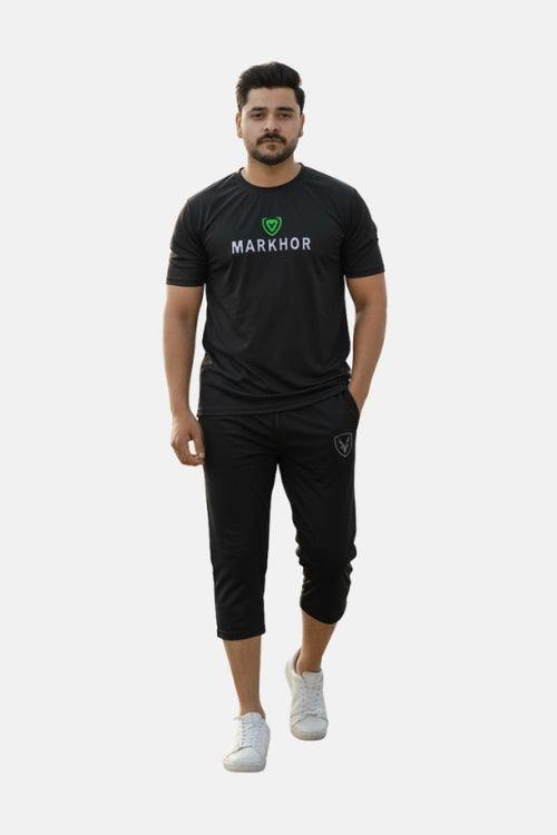 Man wearing a black 'Markhor' branded outfit on a beige background - Black 'Markhour' Tracksuit - Royal Outfits - Track Suits - Black 'Markhour' Tracksuit - Royal Outfits