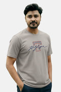 Man wearing a gray t-shirt with a logo on a plain background Light Grey T Hedges T-Shirt Royal Outfits Printed T Shirts - Light Grey T Hedges T-Shirt - Royal Outfits - Printed T Shirts - Light Grey T Hedges T-Shirt - Royal Outfits
