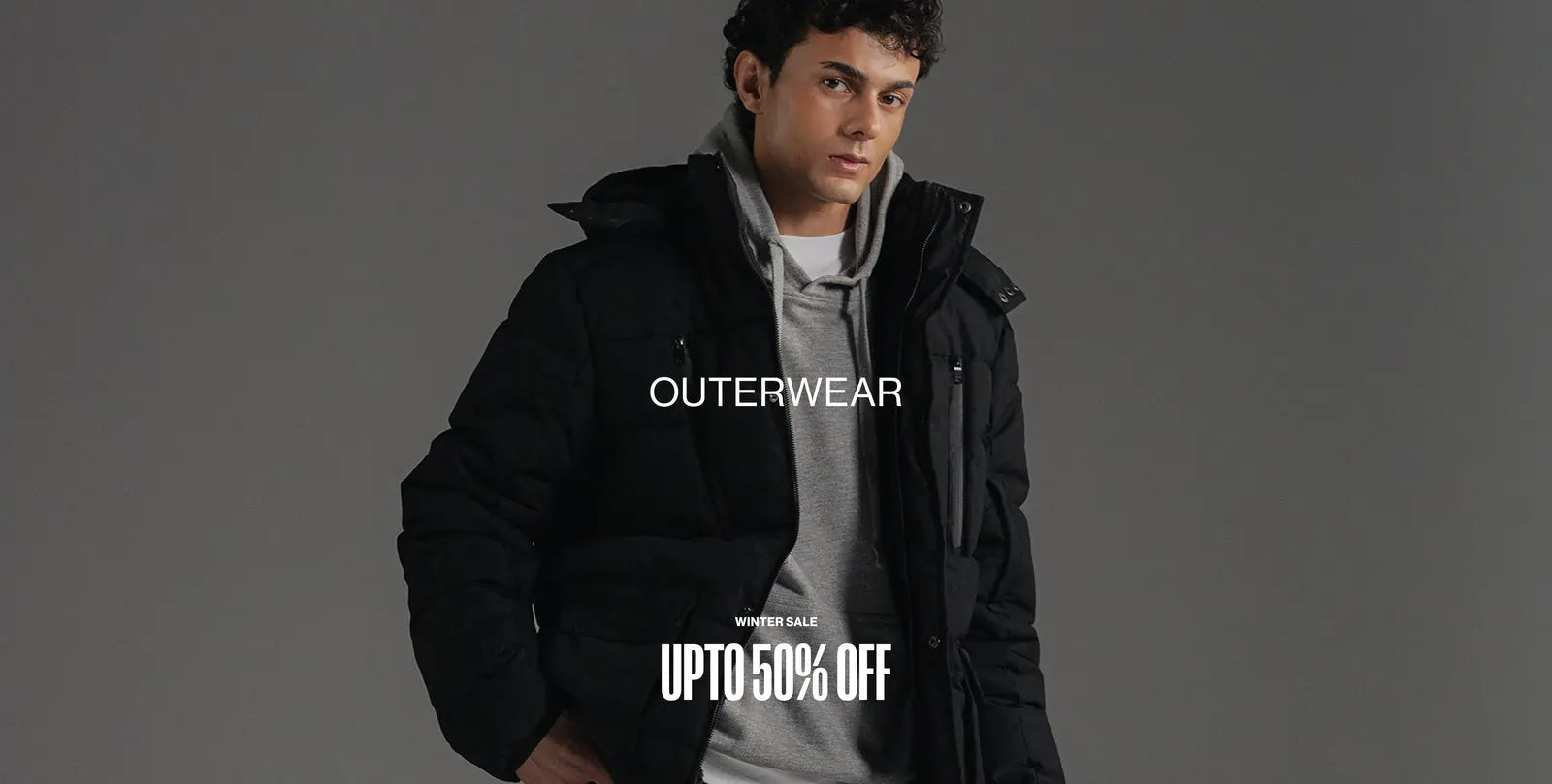 Person wearing a black jacket with promotional text for outerwear on a gray background