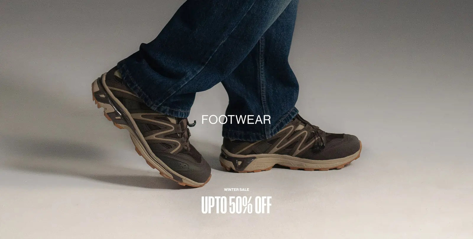 Person wearing dark blue jeans and brown & beige colour shoes with brown & beige soles on a light gray background