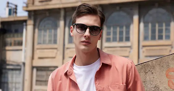 Man wearing sunglasses and a pink shirt in front of a building